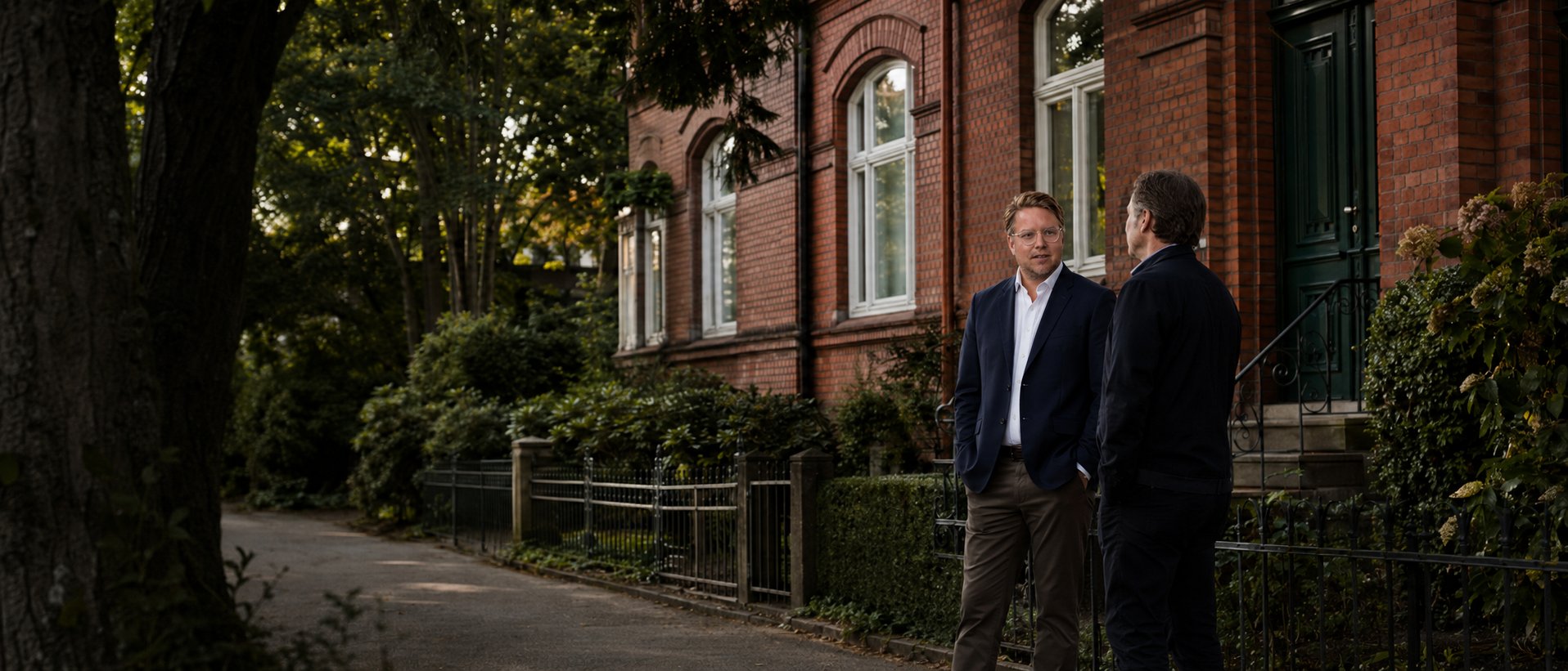 Zwei Berater im Gespräch vor einem Klinker-Altbau